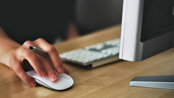 Microsoft 365 licensing Free A hand using a wireless mouse at a modern desk setup with a computer and keyboard. Stock Photo